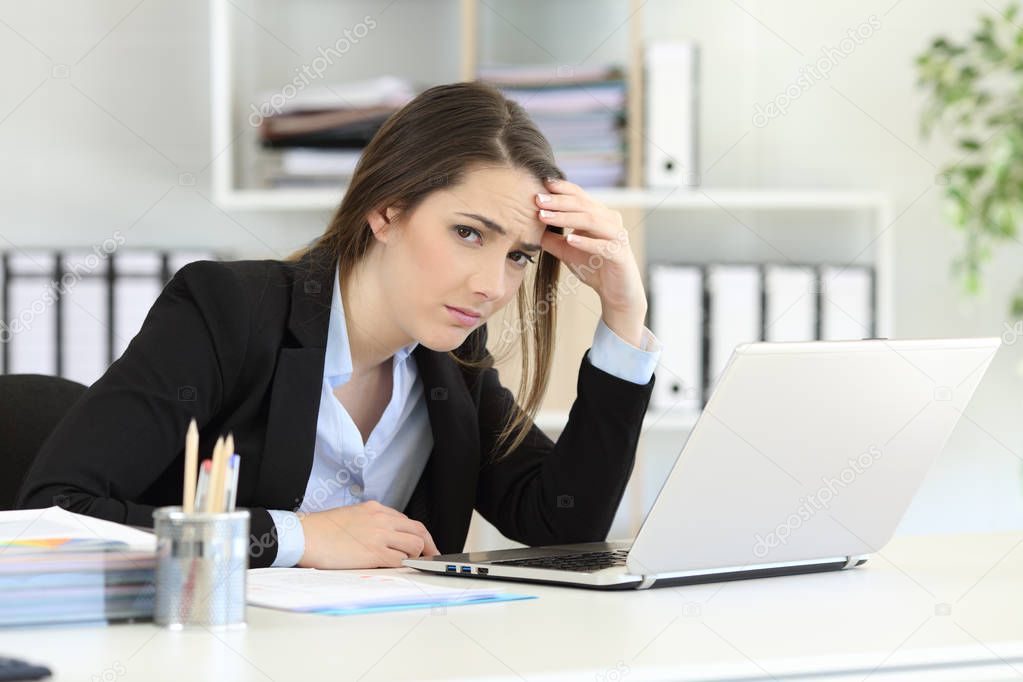 Worried office worker looking at camera sitting in a desktop