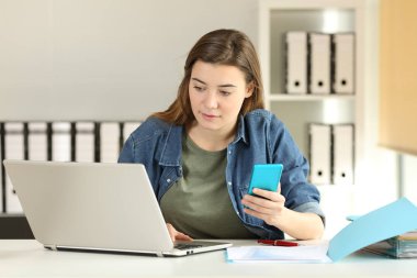 Stajyer bir akıllı telefon ve bir dizüstü bilgisayar üstünde a okul sırası vasıl yazıhane çalışma