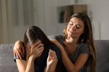 Bad woman is glad about the breakup of a friend sitting on a couch in the living room at home clipart