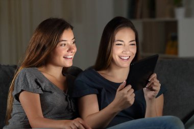 Oturma odasında evde bir kanepede oturan gecede medya içeriği bir tablet izlerken arkadaşlar