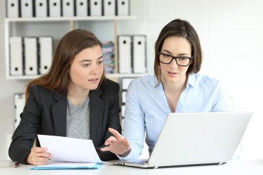 Two concentrated office workers comparing paper documents on-line with a laptop clipart