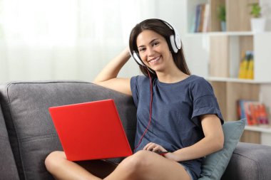 Mutlu teen ile bir dizüstü bilgisayar ve oturma odasında evde bir kanepede oturan kamera bakarak kulaklık