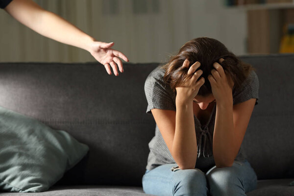 Грустный подросток и рука помощи дома в ночи сидя на диване в гостиной на дому
