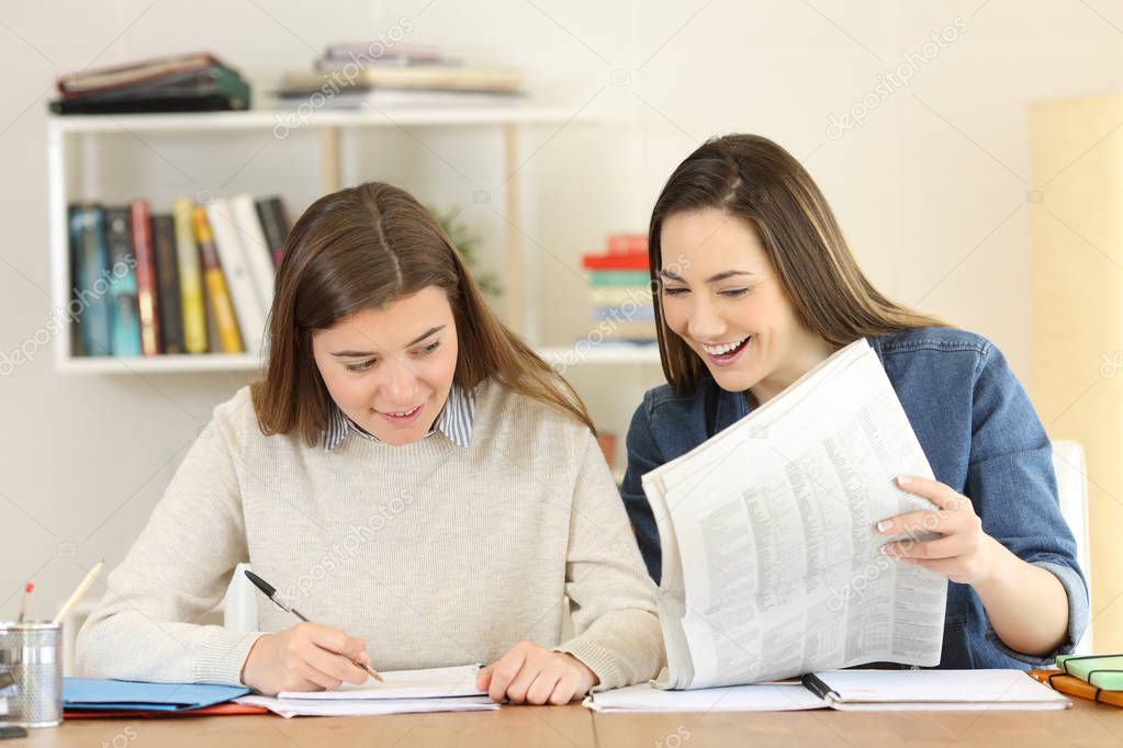 Front view portrait of two students comparing newspaper news at home