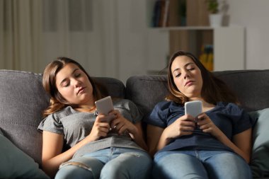 Evde oturma odasındaki kanepede oturan akıllı telefonlarını kullanan sıkıcı arkadaşlar.