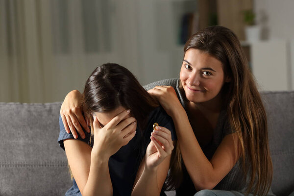 Hypocrite friend comforting a divorced wife sitting on a couch in the living room at home