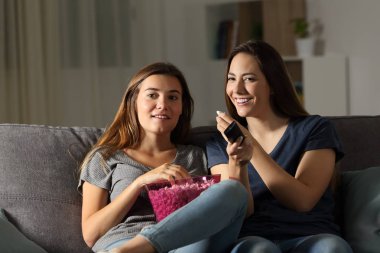 İki mutlu oda arkadaşı wathing tv oturma odasında evde bir kanepede oturan gece