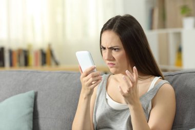 Akıllı telefon oturma odasında evde bir kanepede oturan bakarak kızgın kadın