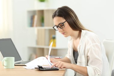 Konsantre ev kadını evde bir hesap makinesini kullanarak muhasebe yapıyor