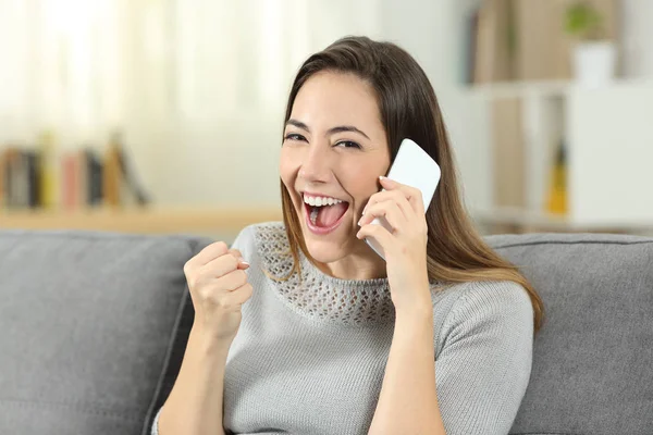 Excited girl receiving good news during a phone call sitting on a couch in the living room at home