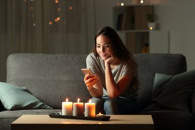 Oturma odasında evde bir kanepede oturan mum ışıkları ile gece telefon kullanan rahat kız