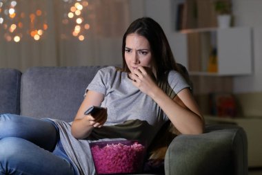Oturma odasında bir kanepede oturan gece evde TV izlerken sinir seyirci