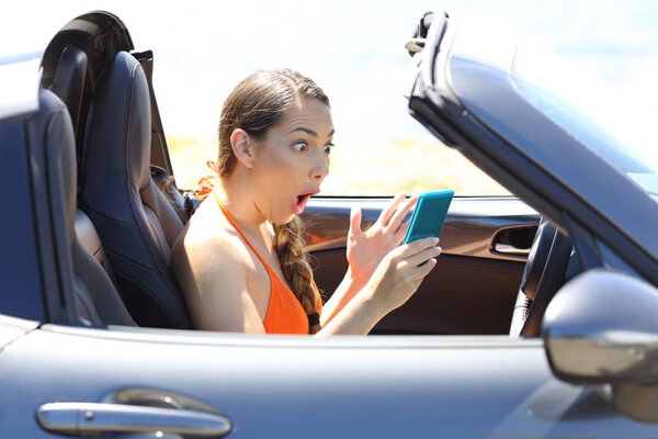 Портрет изумленного водителя автомобиля, смотрящего медиа контент в смартфоне

