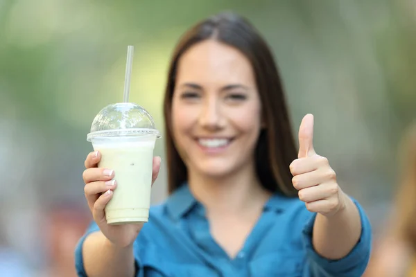 Front view portrait of a satisfied woman holding a smoothie with thumbs up