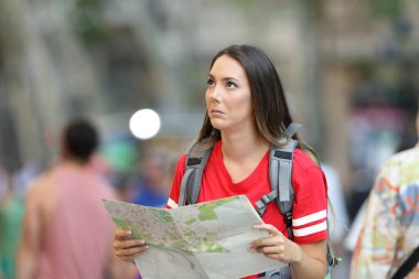 Confused teen tourist holding a paper guide looking above on the street clipart
