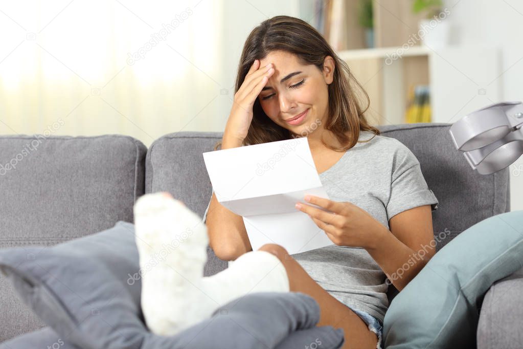 Sad disabled woman reading bad news in a letter sitting on a couch in the living room at home