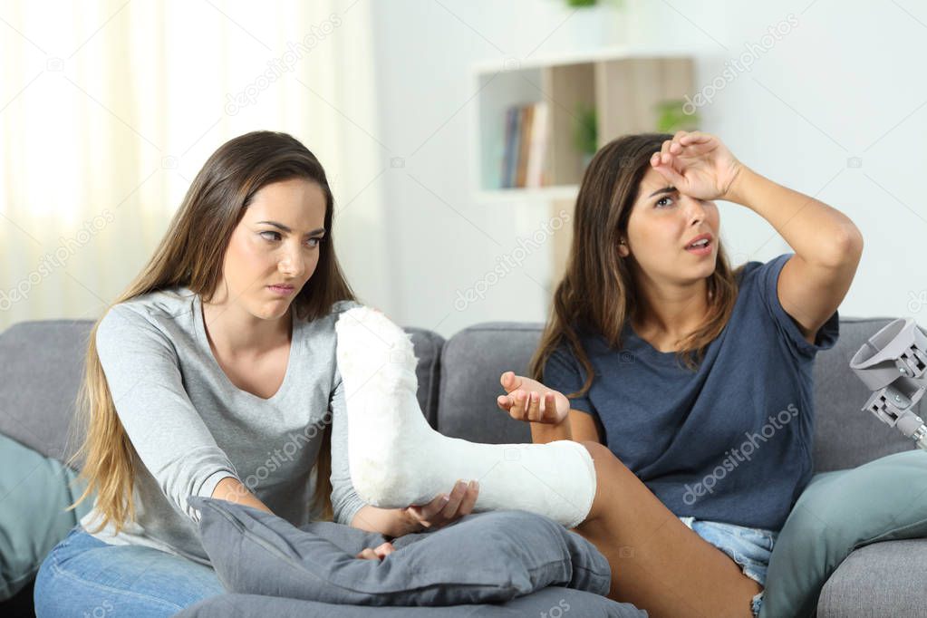 Angry woman helping her dramatic disabled roommate sitting on a couch in the living room at home