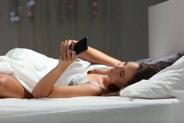 Gece evde yatakta bir akıllı telefon kullanan rahat kadın