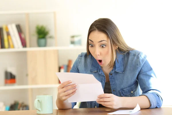 Amazed woman reading surprising news in a letter sitting in a desktop at home