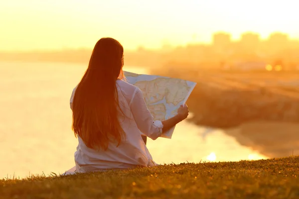 背景の海と夕暮れの芝生に座って紙ガイドを読んで幸せ観光 — ストック写真