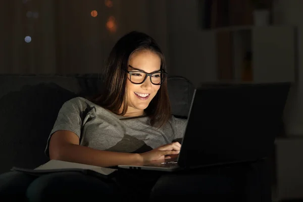夜に自宅の居間でソファに座ってノート パソコンを用いて眼鏡を身に着けている女性 — ストック写真