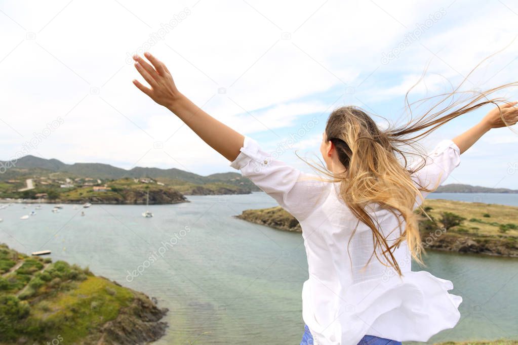 Back view portrait of a happy woman raising arms to the wind