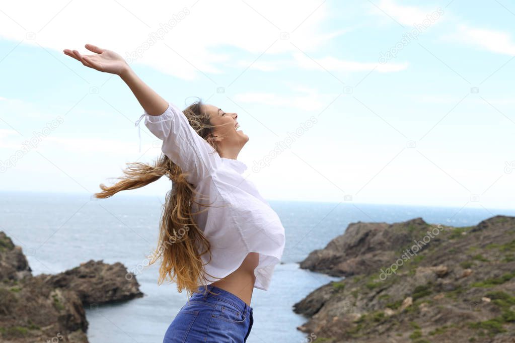 Side view of a joyful girl raising arms to the wind on a coast landscape