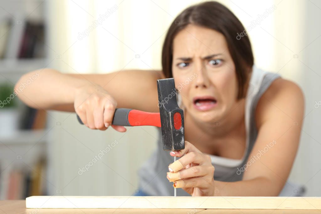 Fronf view of a woman hitting finger with a hammer at home