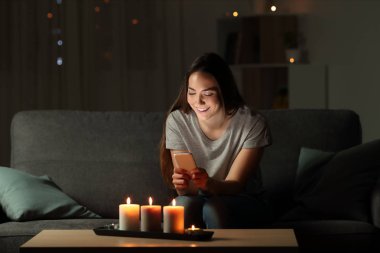 Oturma odasında evde bir kanepede oturan mum ışıkları ile gece bir akıllı telefon kullanan kadın