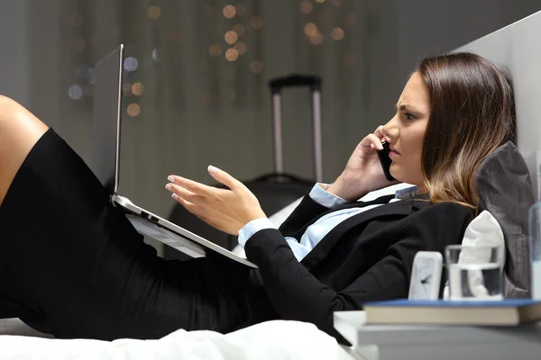 Angry businesswoman complaining on phone on a bed in an hotel room