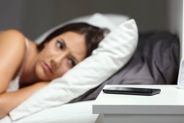 Endişeli kadın bir telefon görüşmesi için bir yatağa gece evde bekliyor.