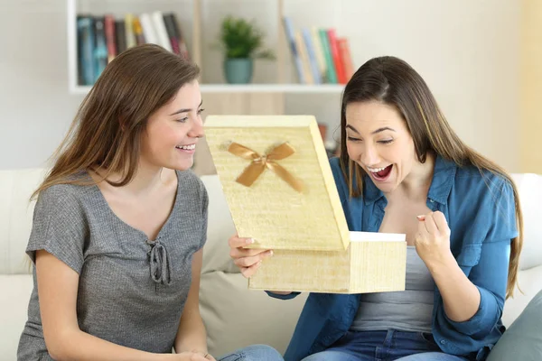 Excited woman receiving a gift from a friend sitting on a couch in the living room at home