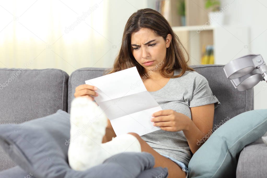 Worried disabled woman reading a letter sitting on a couch in the living room at home
