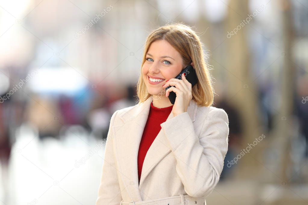 Happy woman having a phone conversation looking at camera in the street in winter