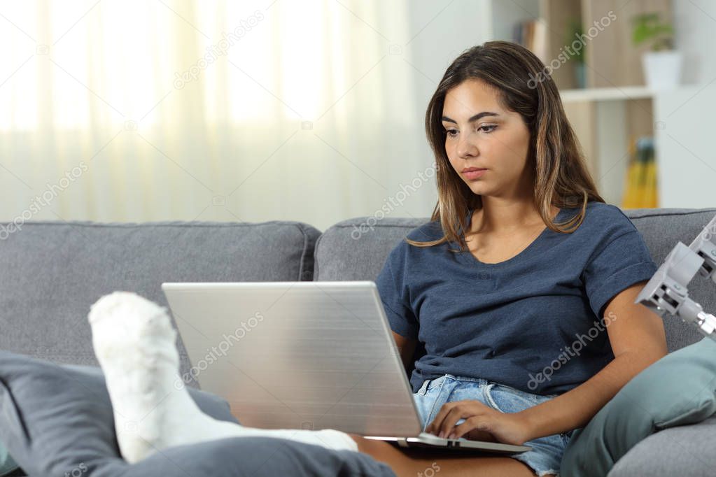 Serious desabled woman using a laptop sitting on a couch in the living room at home