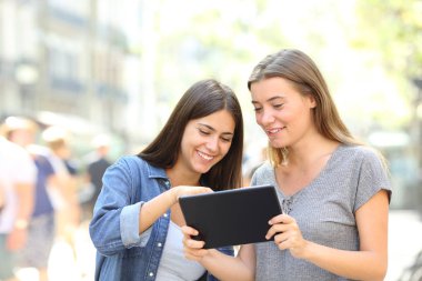 Bir tablet sokakta çevrimiçi içeriği hakkında konuşan iki mutlu arkadaşlar