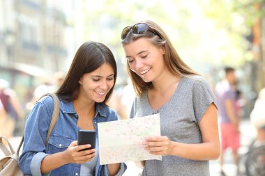 İki mutlu turist danışmanlık bir akıllı telefon ve sokağın ortasında bir kağıt Kılavuzu seyahat