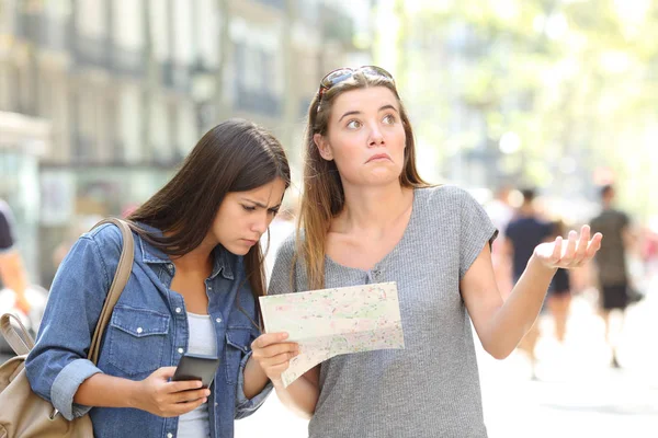 两个迷路的旅游者在街上咨询一张纸地图和一个智能电话搜索位置 — 图库照片