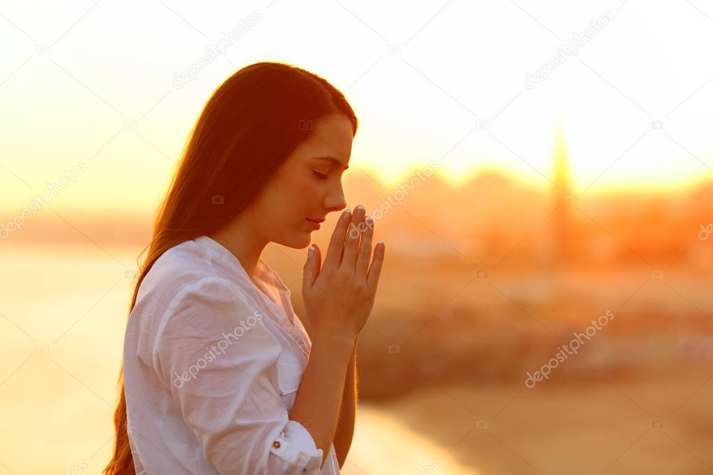 Profile of a concentrated woman praying with hands together at sunset