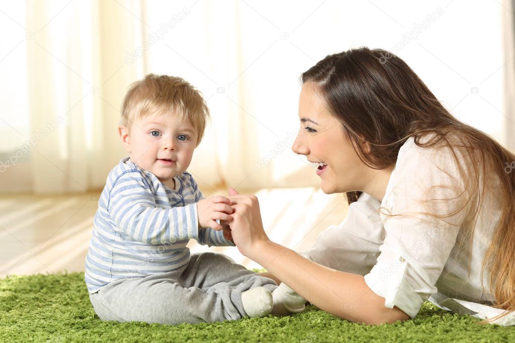Mother playing with her kid that looks at camera on the floor at home
