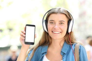 Sokakta boş akıllı telefon ekranını göstermeyi kulaklık ile mutlu bir kız portresi önden görünüm