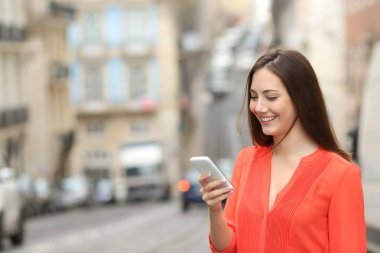 Turuncu mutlu kadın sokakta yürürken bir akıllı telefon kullanır