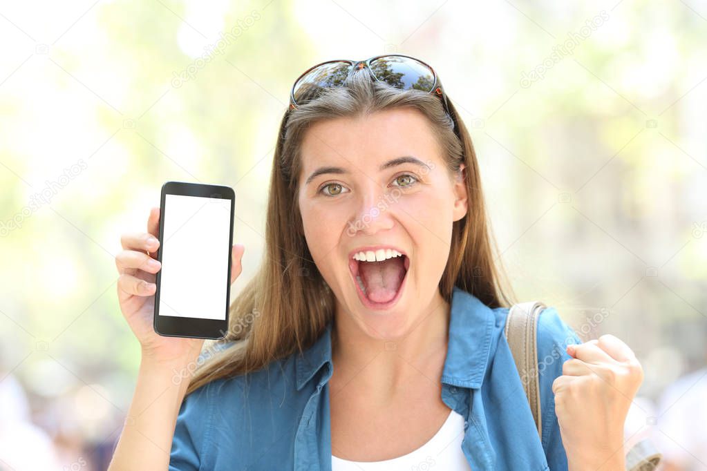 Front view portrait of a excited woman showing a smart phone screen mockup in the street