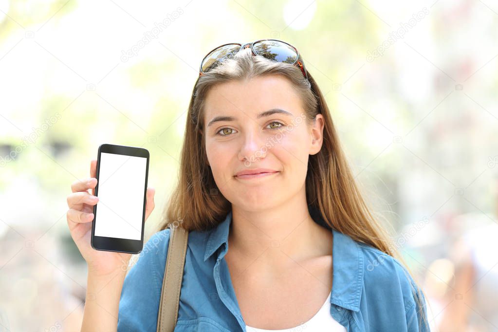 Front view portrait of a satisfied girl showing a blank phone screen in the street