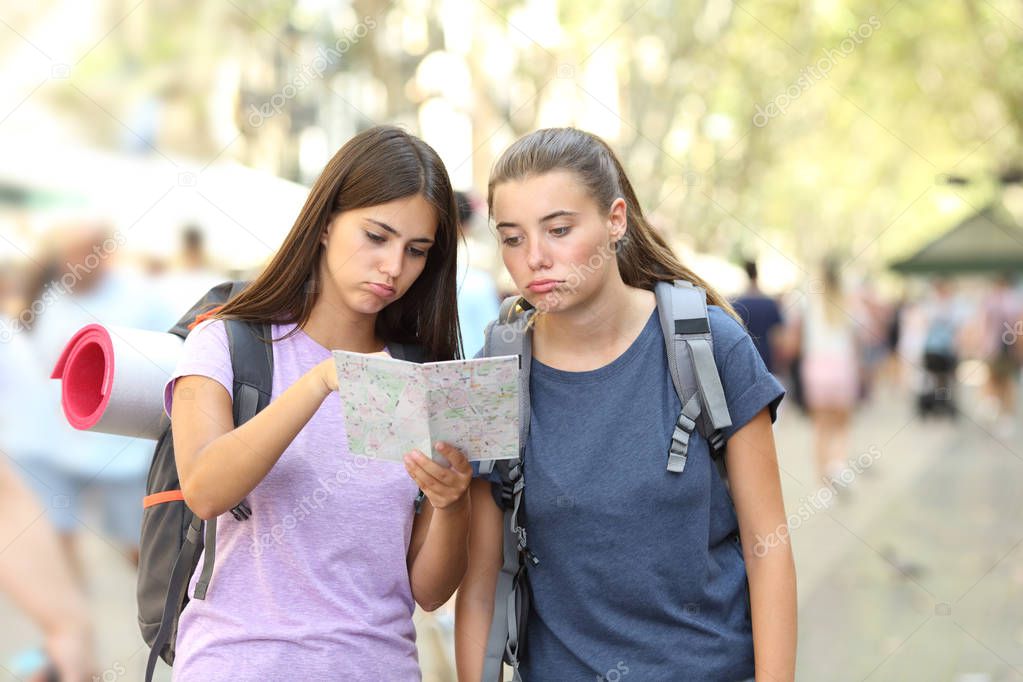 Two bored backpackers searching location in a map in the street
