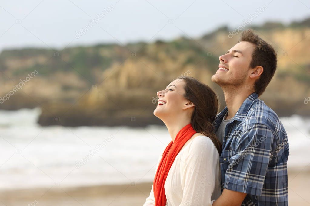 Side view portrait of a happy couple breathing fresh air together on the beach