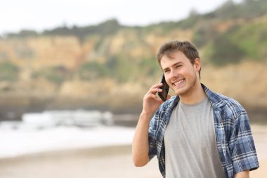 Mutlu genç adam sahilde yürüyüş cep telefonunda bahsediyoruz
