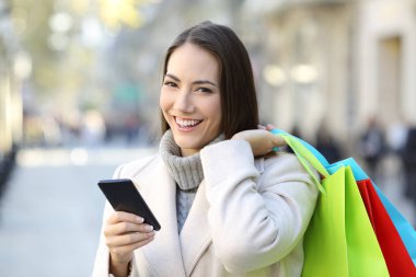 Mutlu müşteri bir akıllı telefon ve renkli alışveriş torbaları sokakta kışın holding