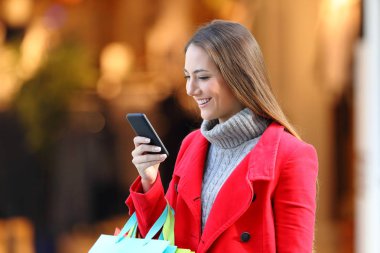 Alışveriş ve bir akıllı telefon kullanarak bir çarşıda kışın mutlu müşteri