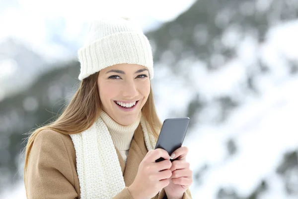 一个女人看着相机拿着电话在冬天在一座雪山上 — 图库照片